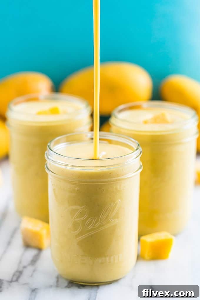 Image showing a luscious mango smoothie being poured into a mason jar, with two more full jars in the soft-focus background.