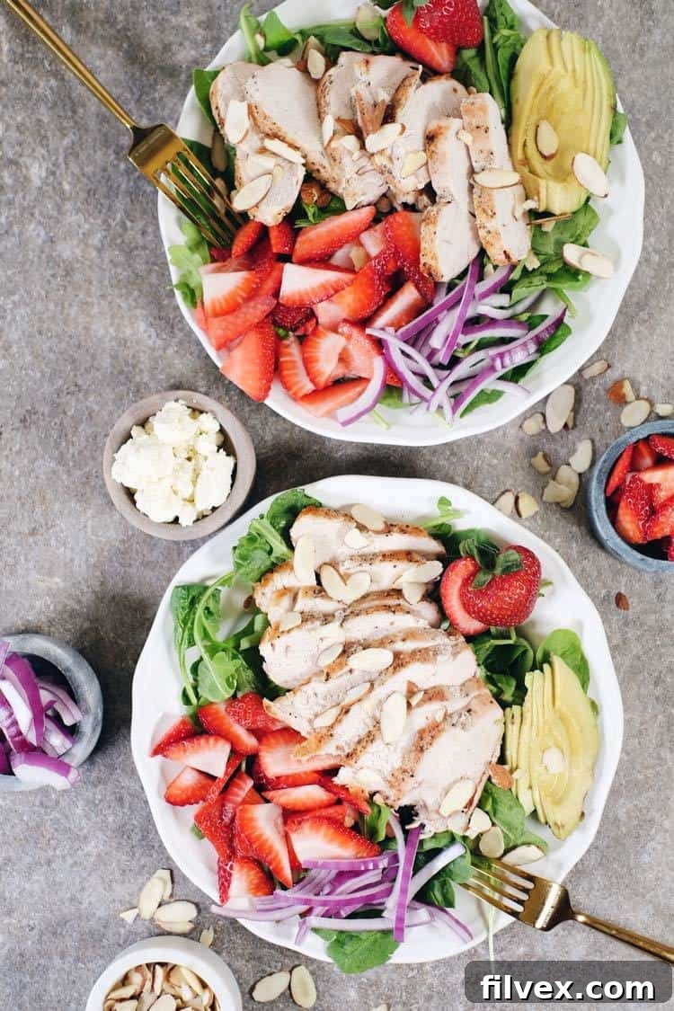 Fresh ingredients laid out for a quick strawberry chicken salad: raw chicken breasts, vibrant spinach and arugula, freshly sliced strawberries, avocado halves, and a red onion, all ready for a speedy meal preparation.