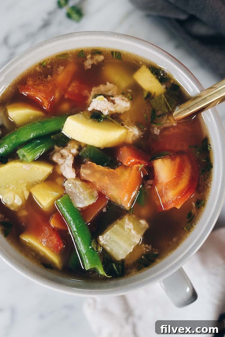 A pot simmering homemade chicken bone broth on the stove, with vegetable scraps and chicken bones, illustrating the process.