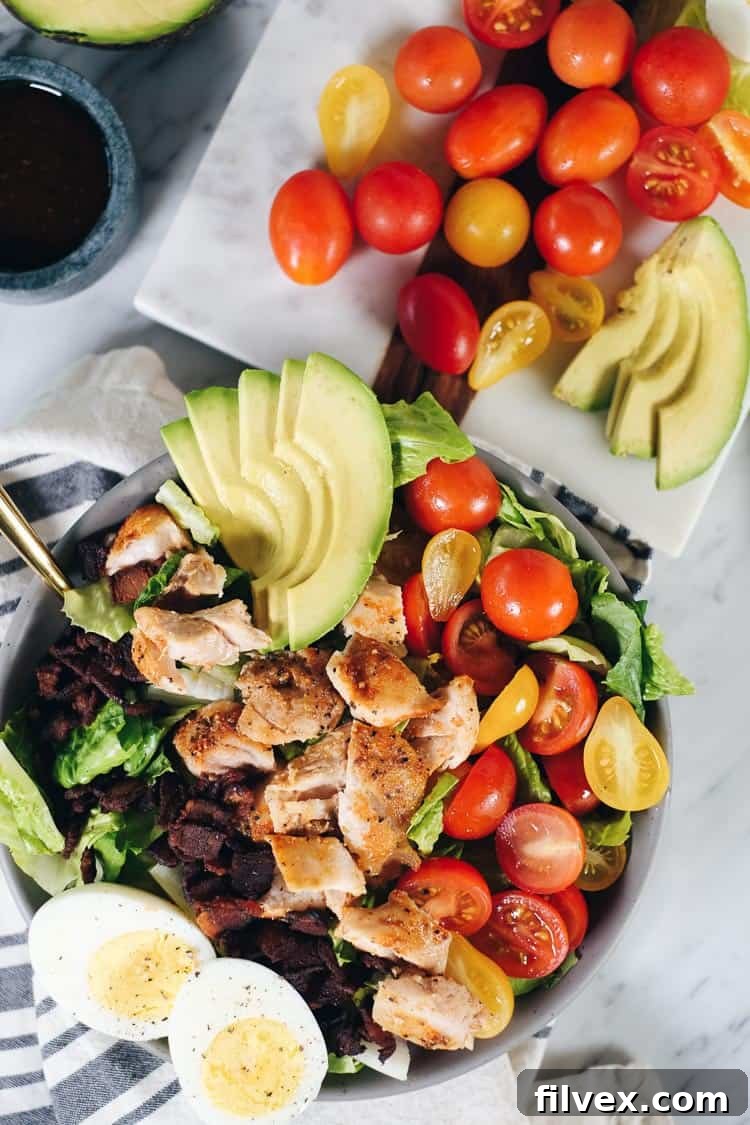 A vibrant close-up of the Easy Paleo Cobb Salad, showcasing smoky bacon, creamy avocado, fresh tomatoes, and chicken with a balsamic dressing, ideal for Whole30.