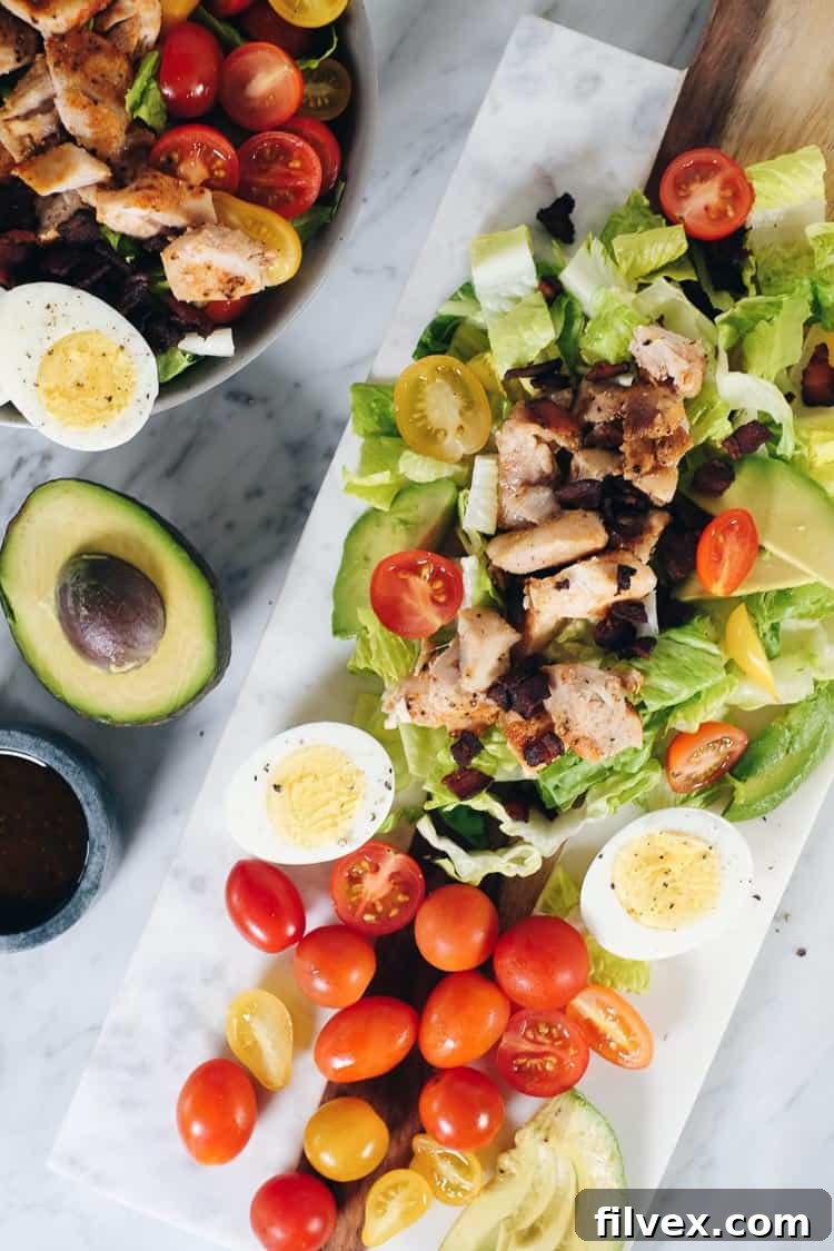 A top-down view of the Easy Paleo Cobb Salad, highlighting the crisp romaine base with perfectly arranged rows of chicken, bacon, avocado, tomatoes, and eggs, ready for the tangy dressing.