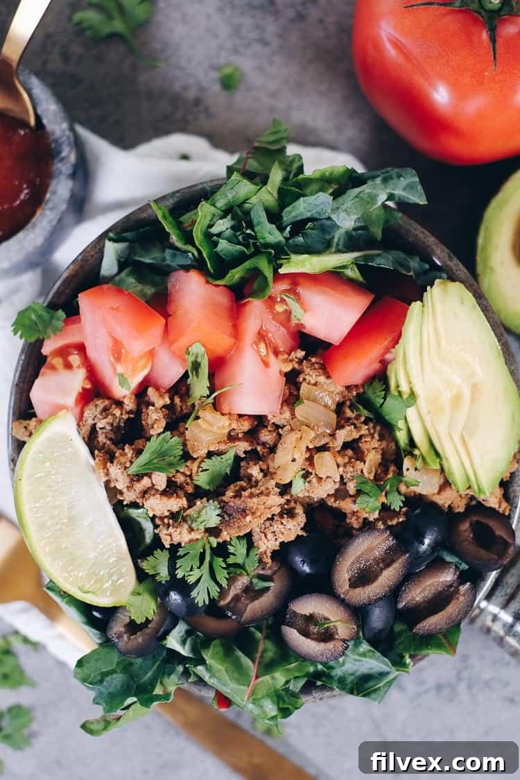 Overhead shot of a healthy Paleo Taco Salad in a white bowl, showcasing seasoned ground meat, fresh greens, avocado, and colorful toppings, suitable for Whole30 and Keto meal plans.