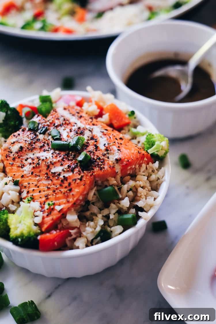 Overhead shot of a beautifully prepared Honey Ginger Salmon Bowl, featuring flaky salmon, a medley of colorful roasted vegetables, and a tantalizing sauce, garnished with fresh green onions and sesame seeds. A healthy and delicious meal option for busy weeknights. | realsimplegood.com