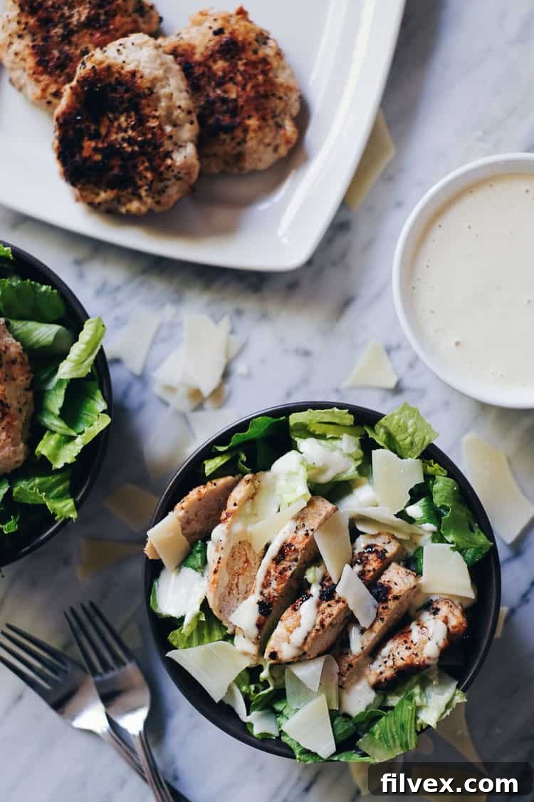 Closeup of perfectly cooked, seasoned ground turkey burgers ready to be served in healthy Caesar salad bowls. Ideal for Paleo, Whole30, and Keto diets.