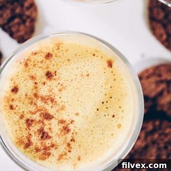 Close-up of a Pumpkin Turmeric Latte in a mug, with foam and cinnamon sprinkle. This recipe is Paleo, Vegan, and Refined Sugar-Free.