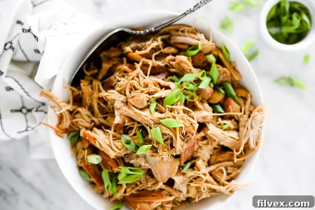 Horizontal image of instant pot honey garlic chicken in a bowl with a serving spoon, topped with chopped green onion. 