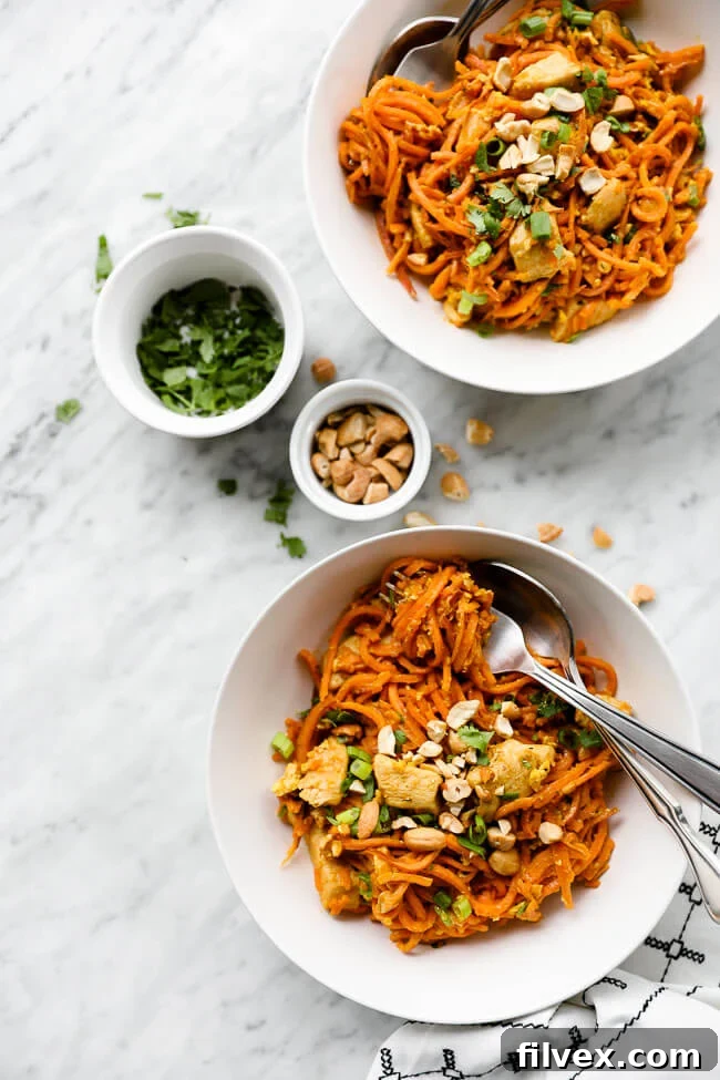 Vertical overhead image showcasing two bowls of Sweet Potato Chicken Pad Thai, garnished with fresh cilantro and chopped cashews, with a fork twirling sweet potato noodles in one bowl. 
