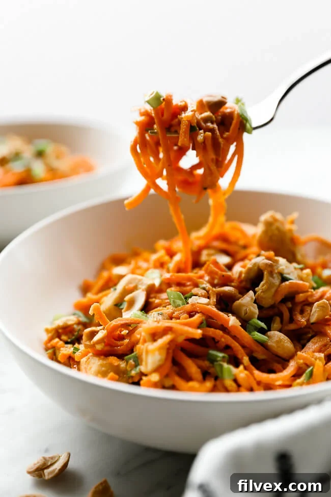 Straight on shot of a perfect bite of Sweet Potato Chicken Pad Thai on a fork, hovering over a full bowl. 