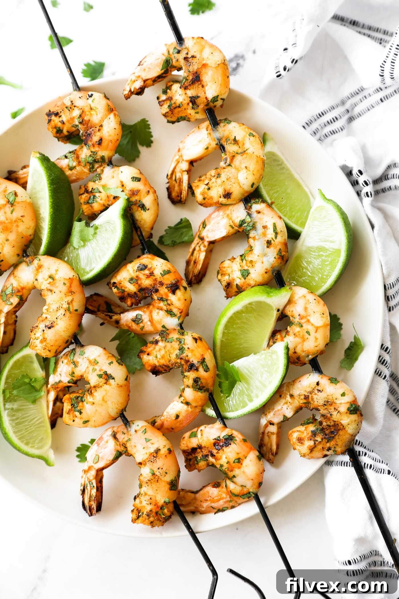 Grilled shrimp kabobs on a plate with lime wedges as a garnish and some fresh chopped cilantro.