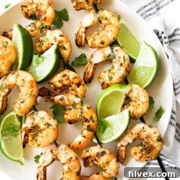 Grilled shrimp kabobs on a plate with lime wedges as a garnish and some fresh chopped cilantro.