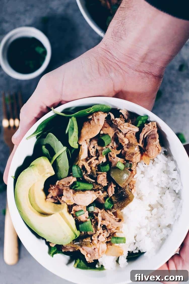 hand holding a white bowl if southwest chicken, greens and rice