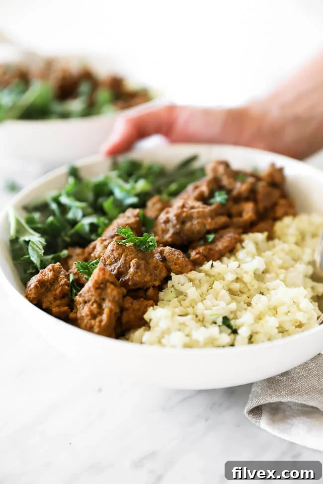 A hand gently placing a beautifully assembled Easy Curry Beef Bowl with cauliflower rice and greens onto a table, ready to be enjoyed.