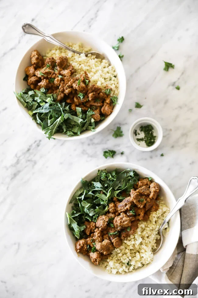 Two enticing bowls of Easy Curry Beef, elegantly presented with crisp greens, fluffy cauliflower rice, and a delicate sprinkle of chopped parsley. Forks are poised for the first delicious bite.
