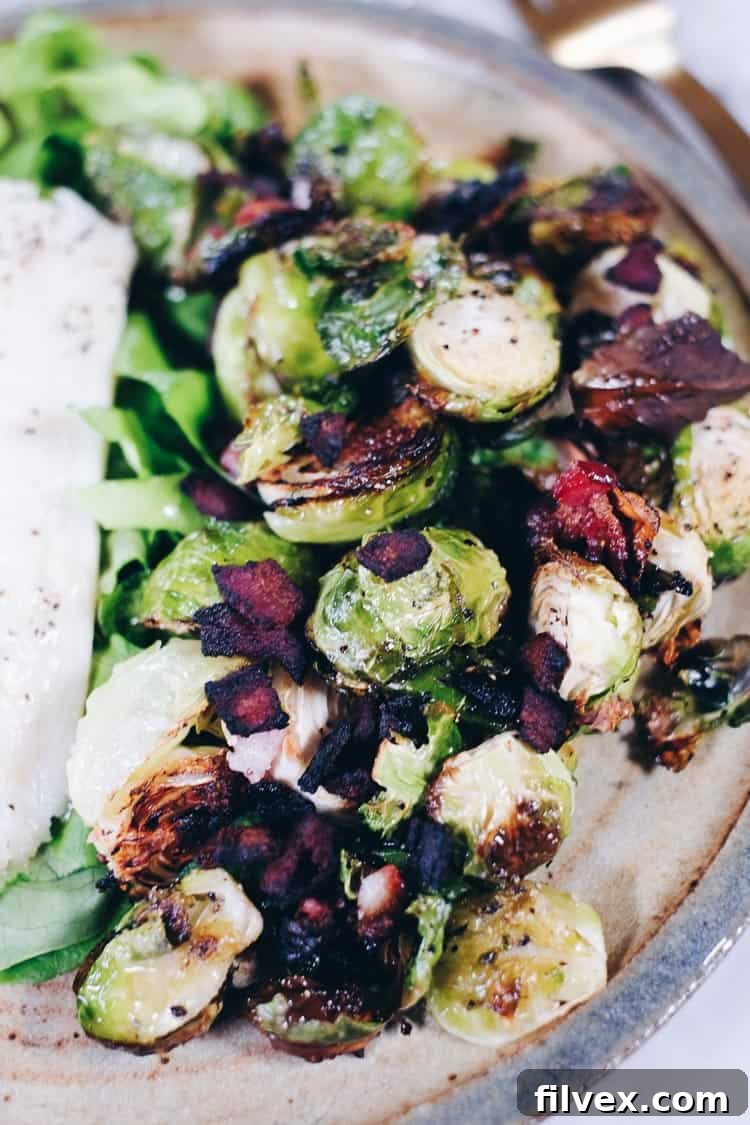 Close-up view of perfectly roasted Brussels sprouts with crispy bacon bits and minced garlic, highlighting their texture and appealing golden-brown edges.