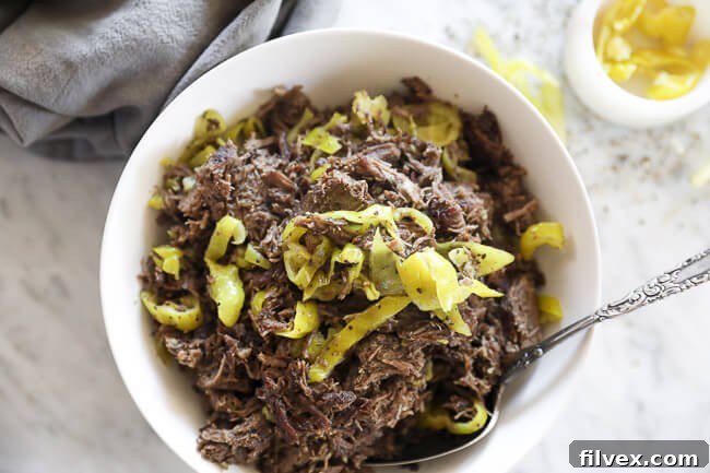 Instant pot italian beef shredded in a bowl with peppers and spoon horizontal overhead image