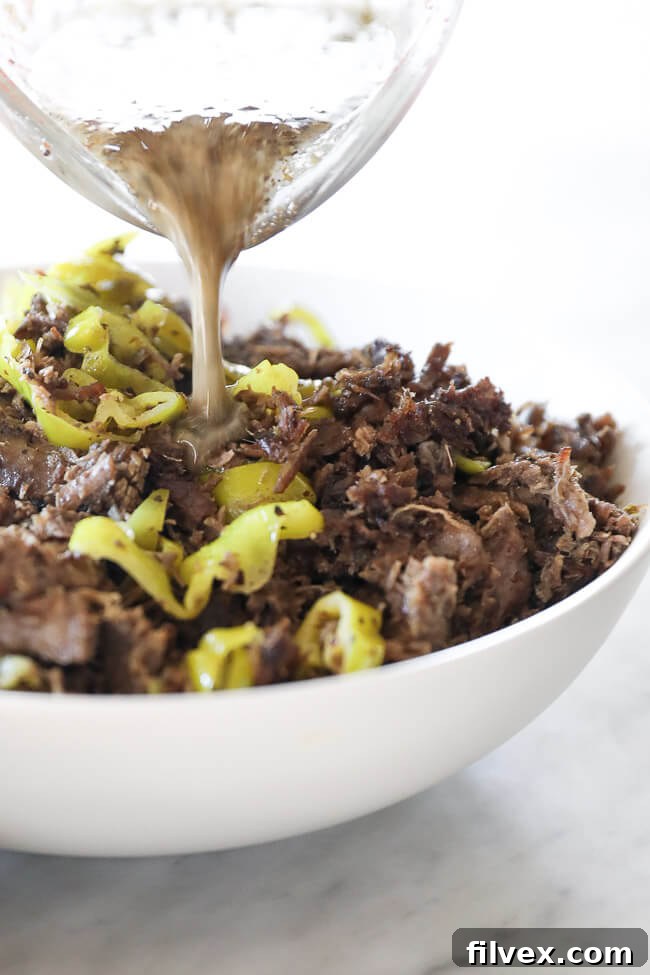 Instant pot italian beef shredded in a bowl with peppers and dressing pouring in close up angle image