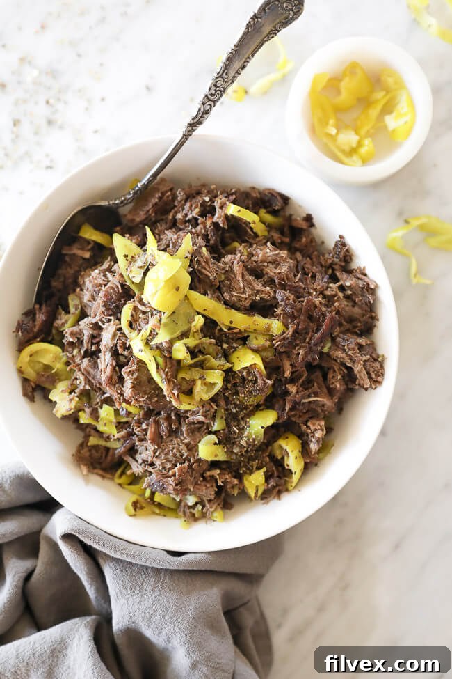 Instant pot italian beef shredded in a bowl with peppers and spoon vertical overhead image