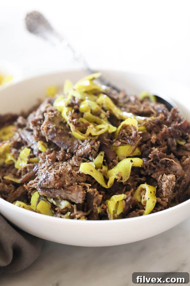 Instant pot italian beef shredded in a bowl with peppers and spoon close up angle image