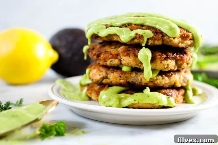 The best salmon patties stacked with green sauce, accompanied by avocado and lemon slices. A healthy and delicious meal.