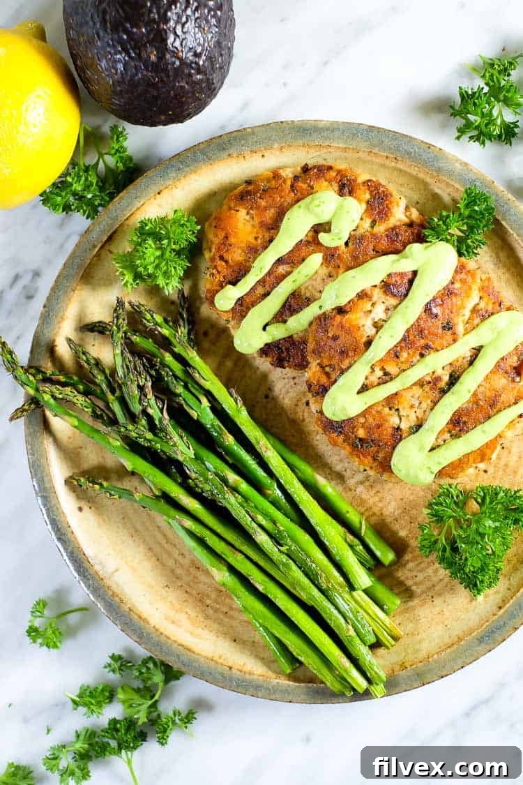 Plated salmon patties with a generous drizzle of green sauce, served alongside fresh asparagus, lemon wedges, and parsley garnish, highlighting a complete meal.