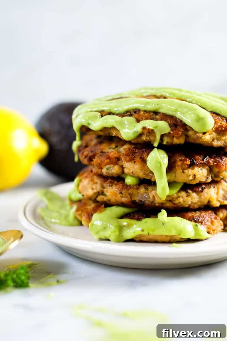 A close-up shot of perfectly stacked salmon patties, beautifully adorned with a cascading drizzle of the vibrant green sauce, emphasizing texture and appeal.