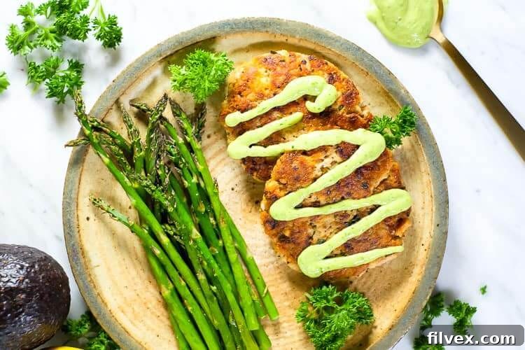Horizontal view of the best salmon patties served with magic green sauce, garnished with fresh asparagus and parsley for a vibrant and appetizing presentation.