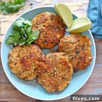Close-up of a stack of golden-brown Sesame Ginger Fish Cakes, garnished with fresh cilantro and lime wedges.