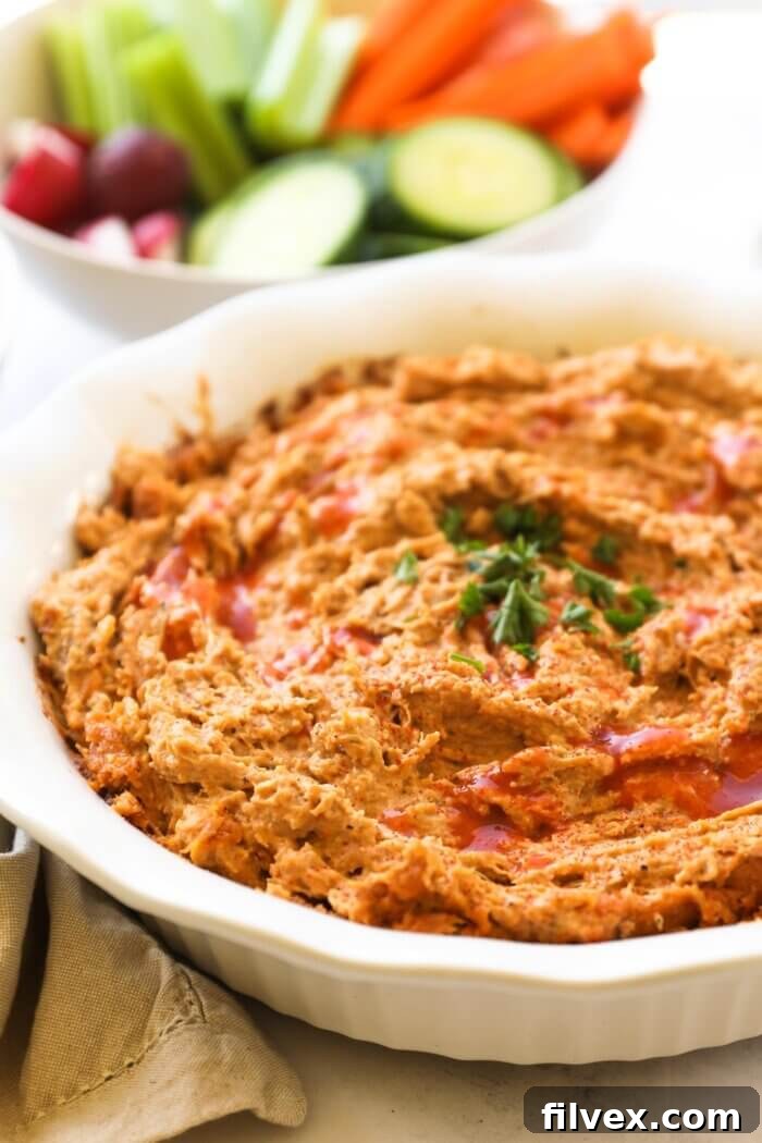 Angled image of a warm dairy-free buffalo chicken dip in a serving dish, beautifully topped with extra hot sauce and fresh chopped parsley for an appealing garnish. The texture is creamy and inviting.