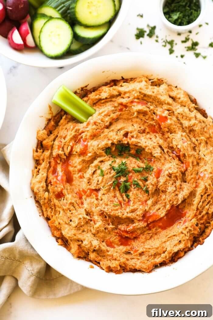 Overhead image of a round baking dish with dairy-free buffalo chicken dip. A little extra hot sauce sprinkled on top, garnished with chopped parsley and a celery stick dug into the dip, ready for serving.