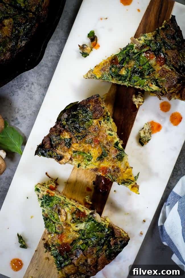 Overhead view of a baked crustless spinach quiche, sliced and ready to serve on a wooden board