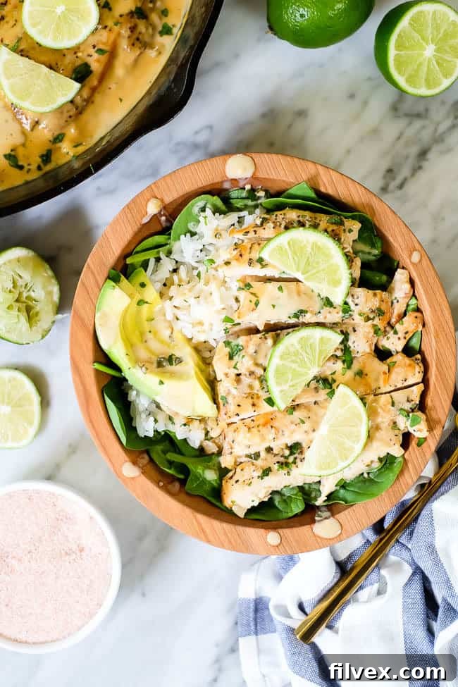 This Paleo and Whole30 friendly coconut lime chicken is so flavorful, fresh and satisfying! Coconut lime chicken in a bowl with spinach, rice, avocado and lime wedges and cilantro on top.