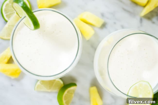 Two glasses of this paleo, dairy-free and refined sugar-free piña colada smoothie garnished with lime slices and pineapple chunks, evoking a perfect summer beverage.