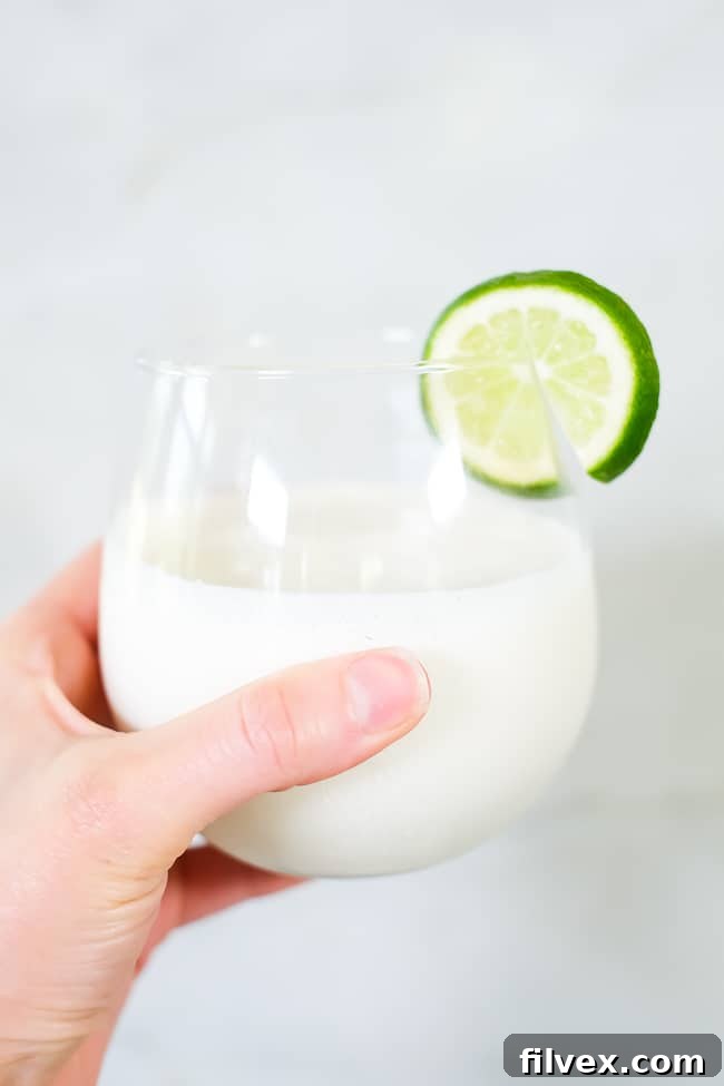 A hand holding a glass of this paleo, dairy-free and refined sugar-free piña colada smoothie, symbolizing a refreshing vacation beverage.