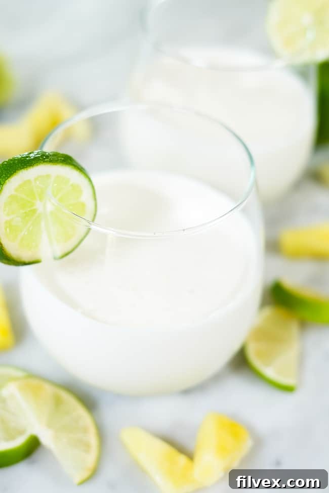 Two glasses of this paleo, dairy-free and refined sugar-free piña colada smoothie garnished with lime slices and pineapple chunks, perfect for a refreshing summer treat.