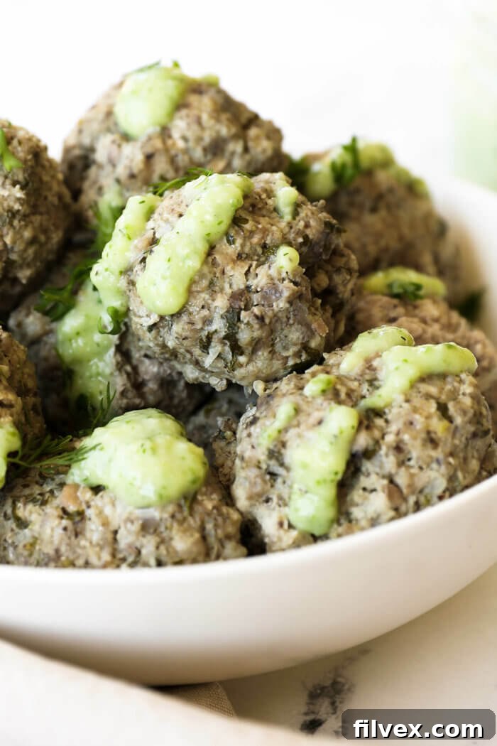 A bowl of fresh, vibrant ingredients including red onion, garlic cloves, parsley, and mint leaves, ready for food processing to make Greek meatballs.