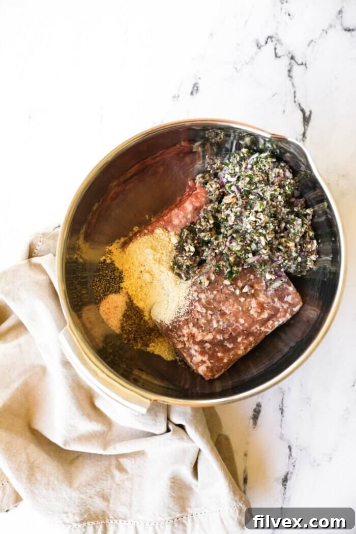 Hands mixing ground meat with finely chopped herbs and spices in a large bowl, preparing the Greek meatball mixture.