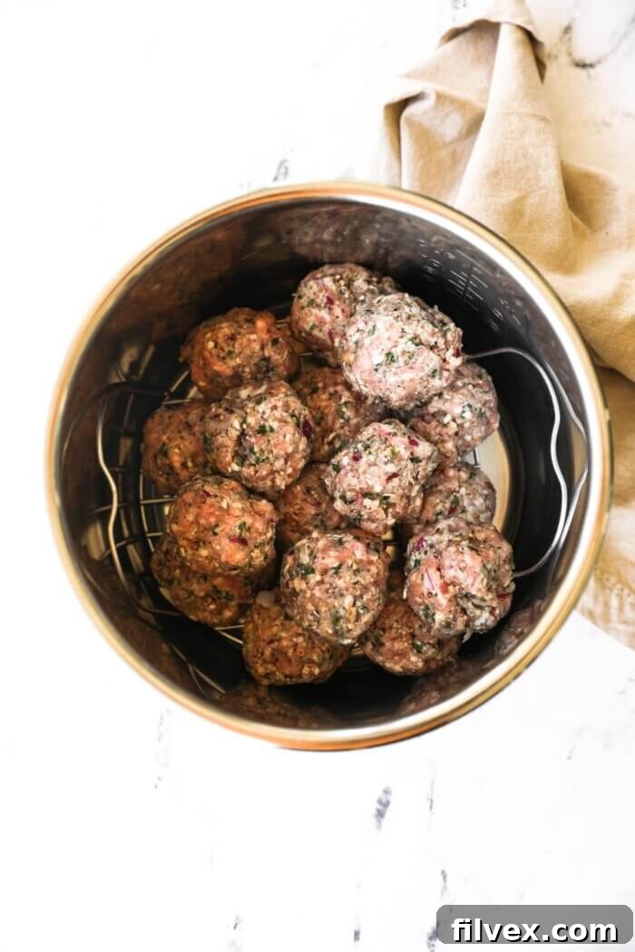 Instant Pot filled with stacked, uncooked Greek meatballs on a trivet, ready for pressure cooking.