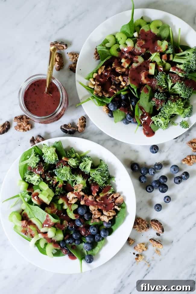 Spinach blueberry salad on plates with extra walnuts and blueberries spread around and blueberry dressing on the side.