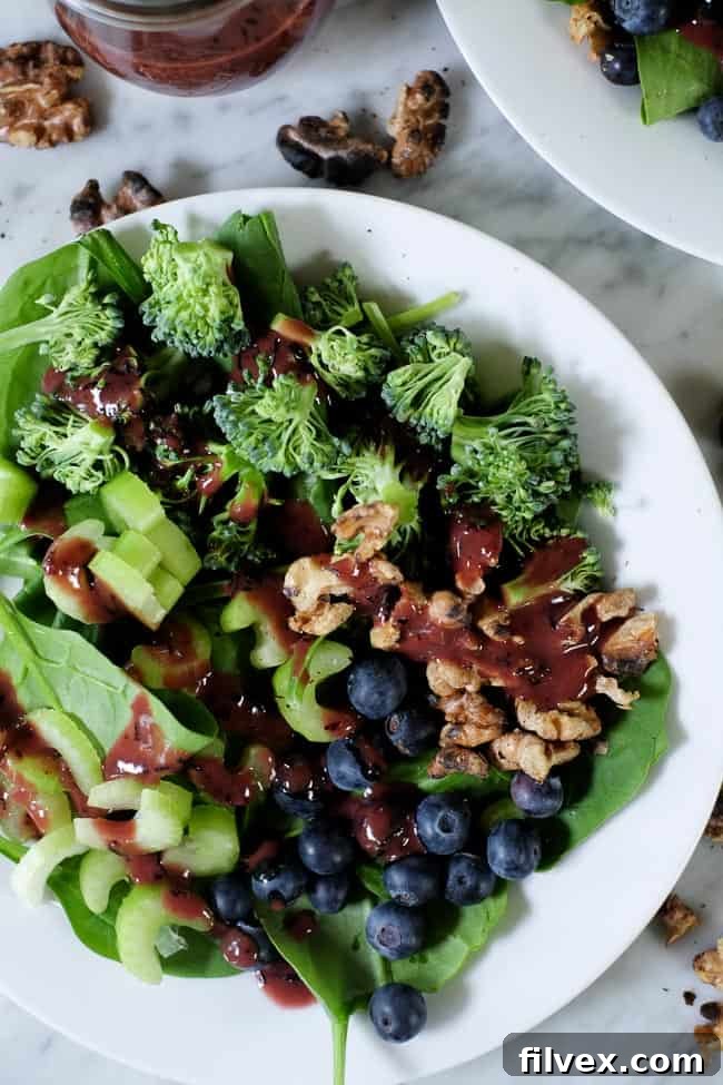 Spinach blueberry salad on plates with extra walnuts and blueberries spread around and blueberry dressing on the side.