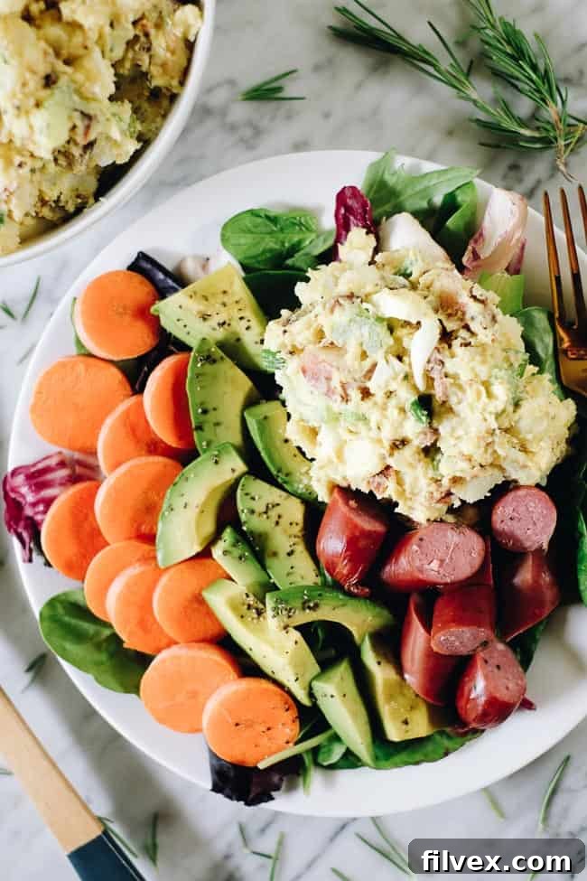 The best potato salad with bacon on a plate with greens, carrots, avocado and sausage. 