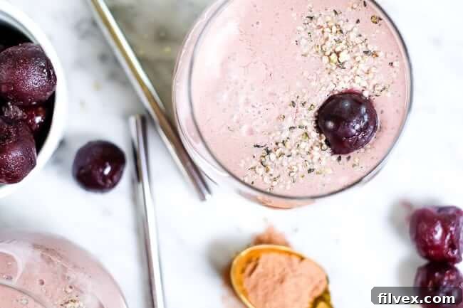 Rich chocolate cherry smoothie in elegant glasses, garnished with a sprinkle of hemp seeds and fresh cherries on top, set against a bright, inviting background.