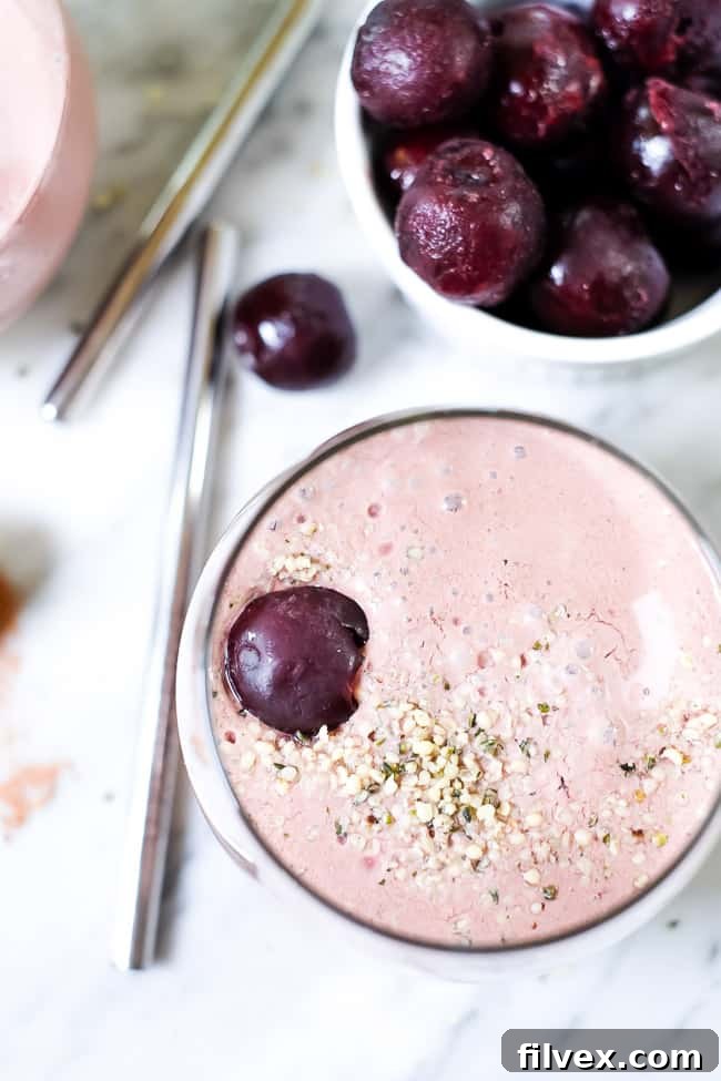 A close-up of the chocolate cherry smoothie in a clear glass, garnished with a sprinkle of hemp seeds and a vibrant red cherry, ready for a refreshing sip.