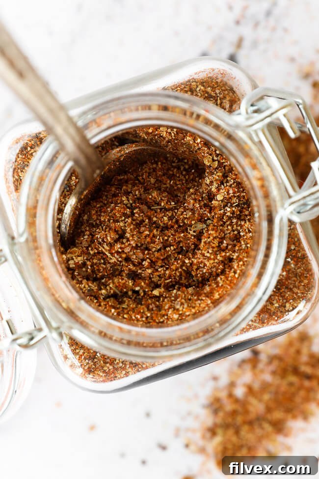 An overhead view of vibrant homemade taco seasoning in a small glass jar, with a wooden spoon scooping out some of the blend