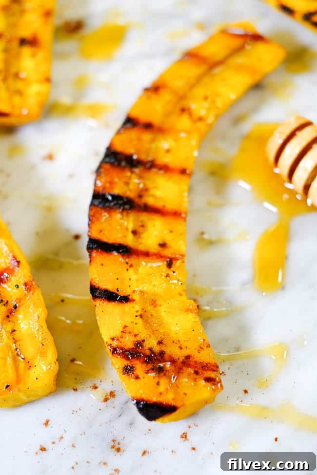 Close-up, angled shot of a grilled plantain adorned with honey and cinnamon, showcasing its golden-brown char and inviting texture.