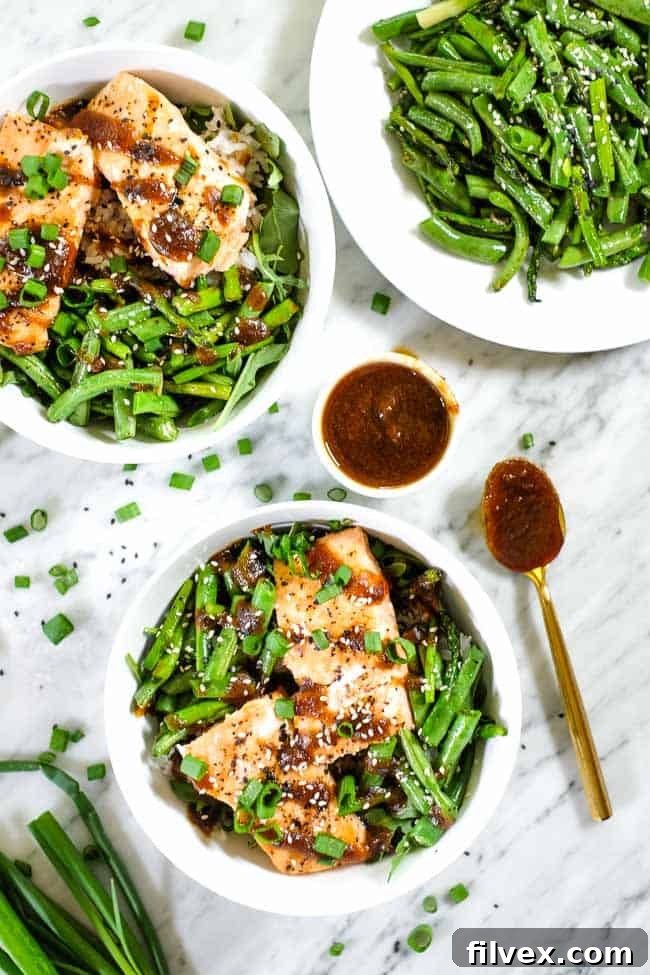 Grilled teriyaki salmon in a bowl with green beans, asparagus, rice and greens. Topped with teriyaki sauce, green onion and sesame seeds. 