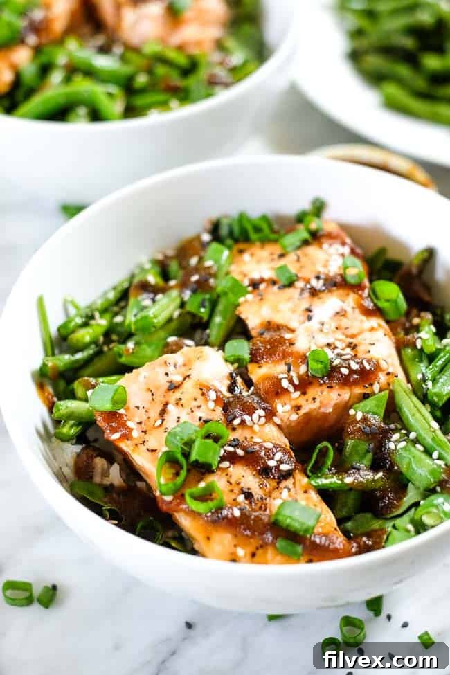 Grilled teriyaki salmon in a bowl with green beans, asparagus, rice and greens. Topped with teriyaki sauce, green onion and sesame seeds. 