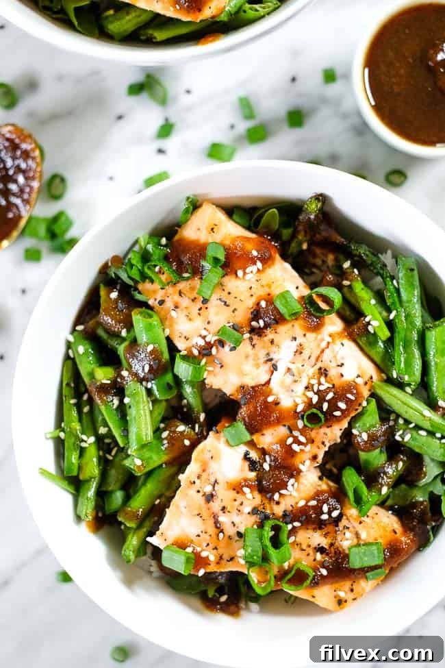 Grilled teriyaki salmon in a bowl with green beans, asparagus, rice and greens. Topped with teriyaki sauce, green onion and sesame seeds. 