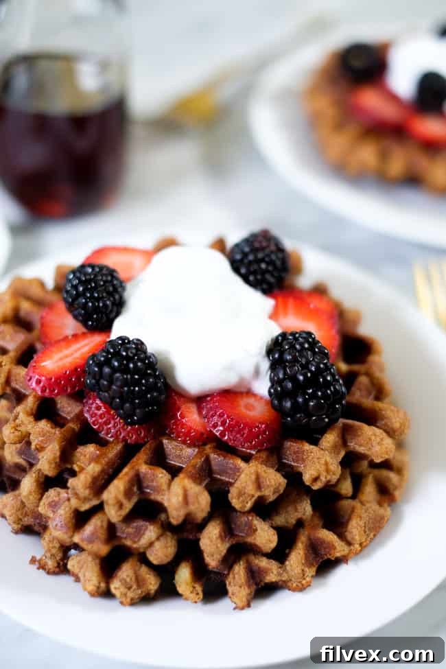 A beautiful stack of Paleo waffles, generously topped with fresh berries and a dollop of creamy coconut whipped cream, ideal for a wholesome breakfast.