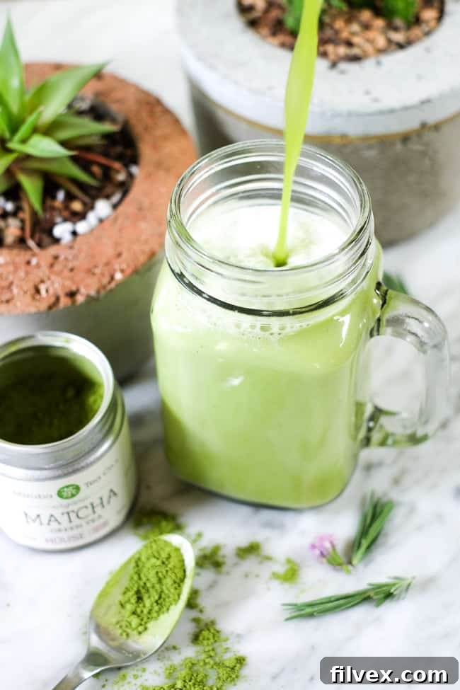 Pouring iced matcha latte into mason jar mug with succulents in the background. 