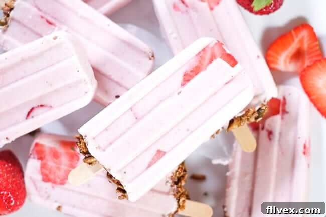 Vibrant creamy strawberry popsicles, featuring a delightful granola base and garnished with fresh strawberries